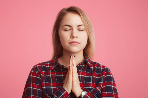 istock Faithful pretty female model keeps palms pressed together, closes eyes, has big hope for better and improvement her bad situation in life, isolated over pink background. Peaceful atmosphere. 902609572