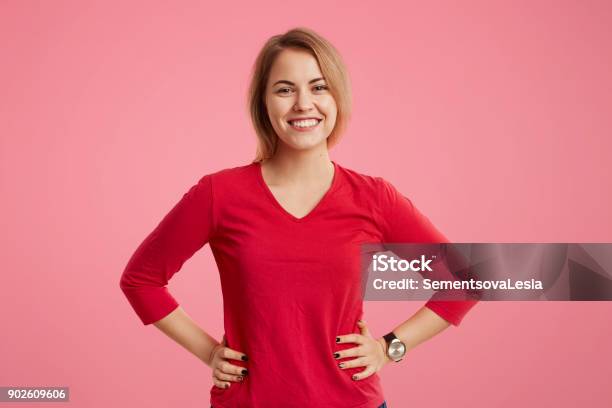 Waist Up Portrait Of Cheerful Slim Beautiful Woman Keeps Hands On Waist Dressed In Fashionable Clothes Has Pleasant Smile With White Perfect Teeth Isolated Over Pink Background Emotions Concept Stock Photo - Download Image Now