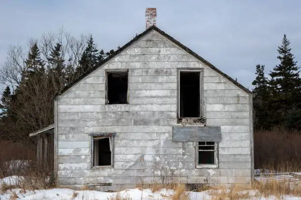 An abandoned house. Windows are missing. Side in very poor condition. Woods in background.