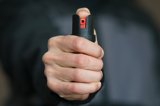 Man holding pepper spray (tear gas) in his hand. Self-defense. Blur background, close up.