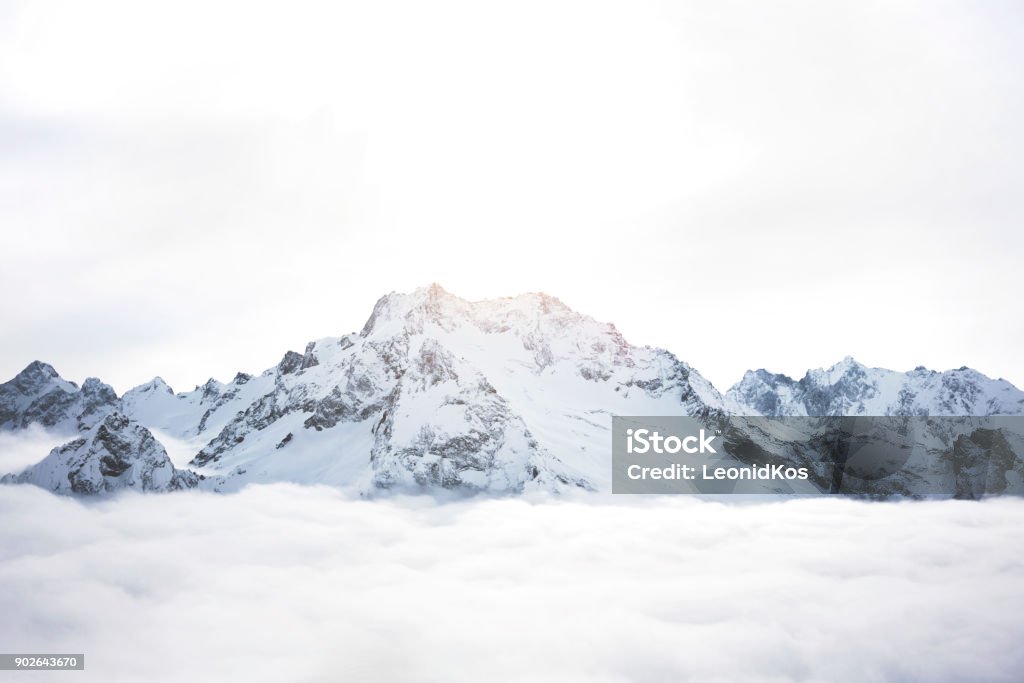 Montagne innevate sopra le nuvole. Grande massiccio invernale di rocce - Foto stock royalty-free di Montagna