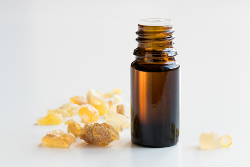 A dark bottle of frankincense essential oil with frankincense resin on a white background
