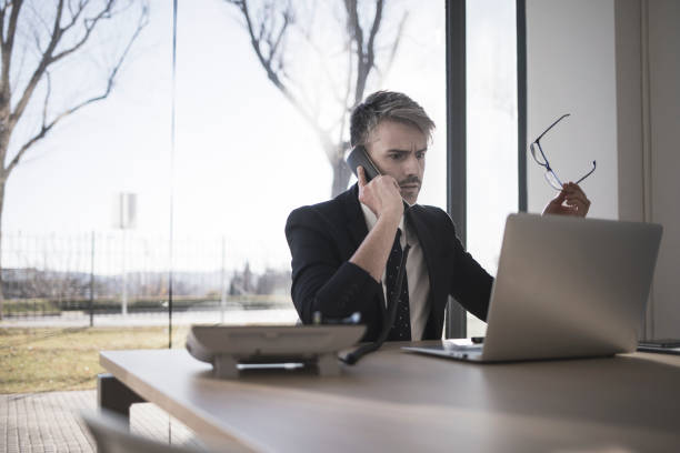 istock Angry businessman talking on the phone and looking at laptop computer 902643964