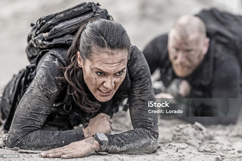 Redhead male and brunette female military swat security anti terror duo crawling  together during operations in muddy sand Sports Training Stock Photo