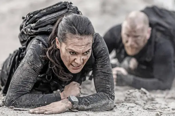 Redhead male and brunette female military swat security anti terror duo crawling  together during operations in muddy sand