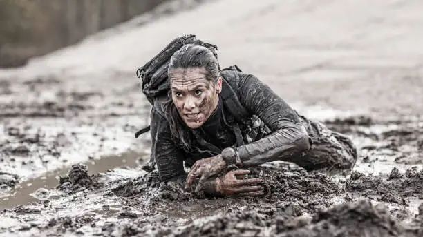 Photo of Beautiful brunette female military swat security anti terror agent crawling during operations in muddy sand