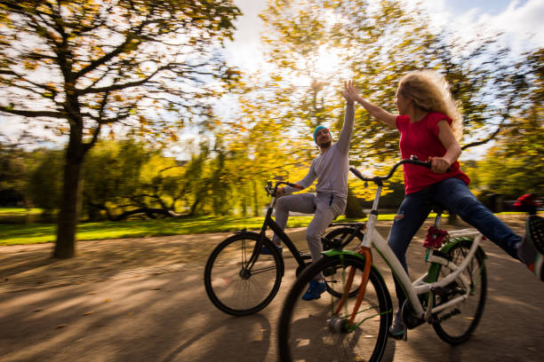 happy young couple riding bikes and doing hay five in nature at sunny day. - dutch ethnicity imagens e fotografias de stock