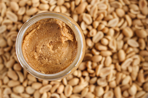 Peanut butter in jar on peanuts background