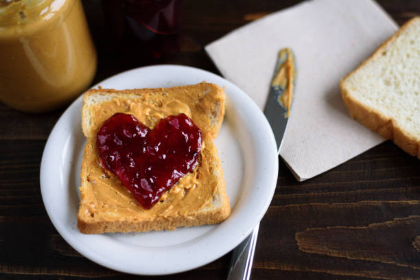 Peanut butter and heart shaped jelly sandwich Peanut butter and heart shaped jelly sandwich on wooden background peanut butter and jelly sandwich stock pictures, royalty-free photos & images