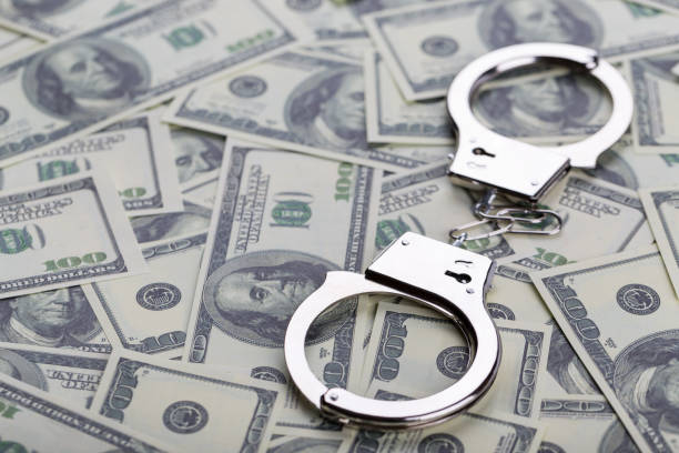 istock Pair of handcuffs closeup on dollar banknotes background 902663366