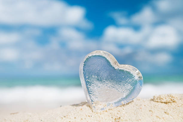 istock clear glass heart on white sand beach, 902663382