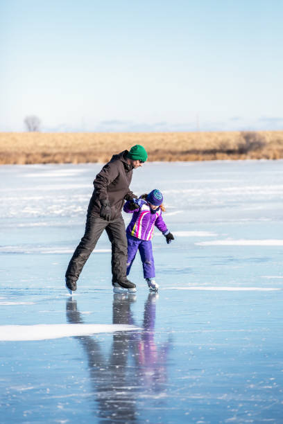 father helping daughter learn how to skate on frozen lake - ice skates imagens e fotografias de stock