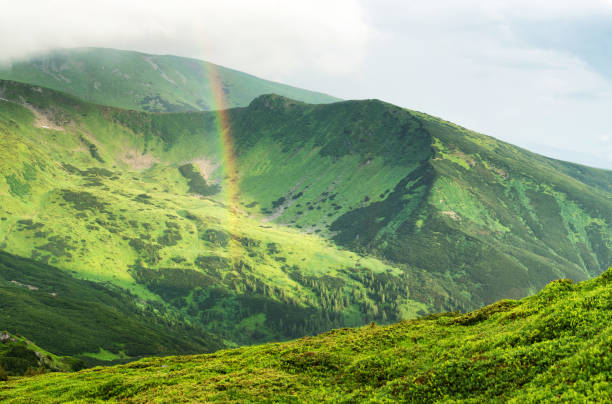 Rainbow under mountain ridge. Panoramic landscape in the summer time