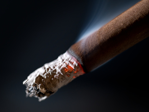 Burning brown cigar with smoke extremal close up. On abstract black background