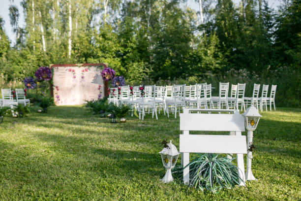 istock Beautiful setting for outdoors wedding ceremony waiting for bride and groom and guests. White chairs decorated with flowers, are in the zone of the wedding ceremony in a forest. copy space 902693708