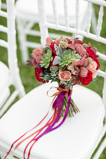 Stunning red bridal bouquet on white chair. Wedding ceremony. Mix of succulents, orchids and roses.
