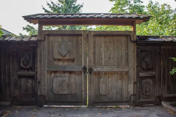 Old wooden gate with ornaments and a small roof with wickets on either side of them. Photos near