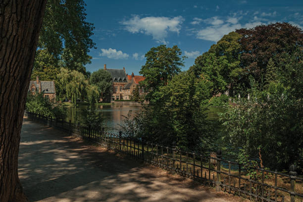 istock Path amidst greenery, lake and old brick building on the other side in Bruges. 902706570