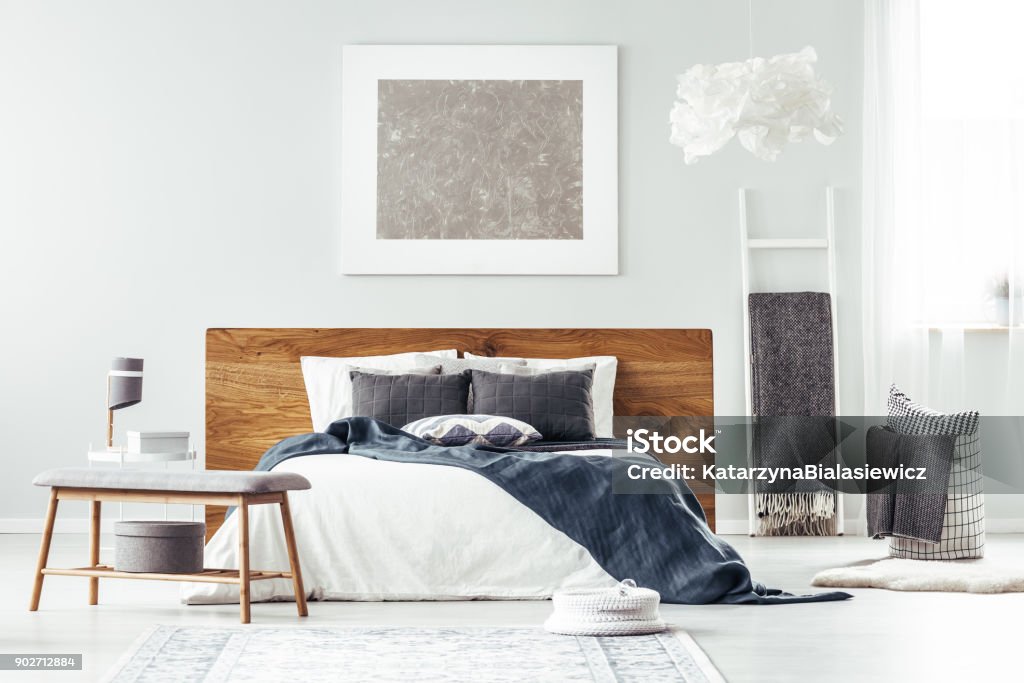 White bed in bedroom interior Navy blue blanket on white bed with wooden bedhead and large, silver painting on the wall in bedroom interior Lifestyles Stock Photo