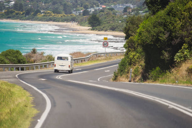 Volkswagen Kombi van driving down Great Ocean Road Lorne, Australia - January 3, 2018: A Volkswagen Kombi (or Transporter) van driving down Great Ocean Road, with Lorne Beach in the background. lorne stock pictures, royalty-free photos & images