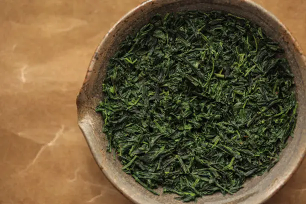 Japanese gyokuro green tea leaves in a Tokoname clay shiboridashi-style teapot on a washi paper background.