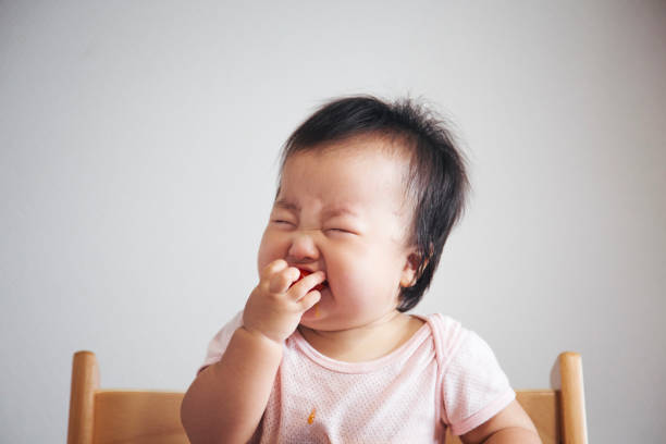 Baby's surprised face just after she ate tomato for the first time in her life Japanese baby girl making grimaces since tomato which she ate was sour. grimacing photos stock pictures, royalty-free photos & images