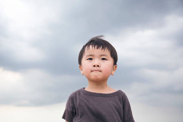 Boy standing under a cloudy sky Portrait of Japanese boy. determination asian stock pictures, royalty-free photos & images