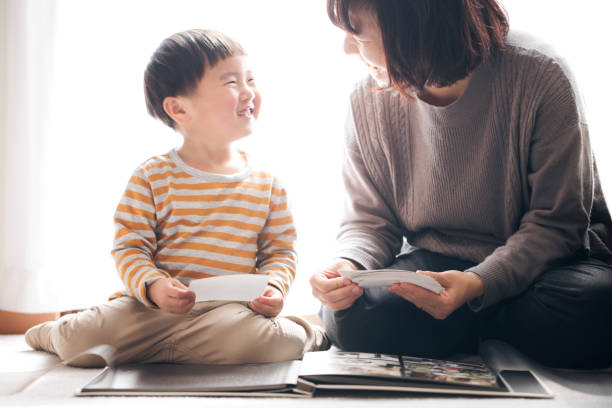 Mother and son smiling together while making photo album Japanese mother and son putting photographs on photo album together. life events photos stock pictures, royalty-free photos & images
