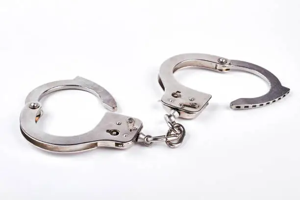 Photo of Pair of metal handcuffs over white background.