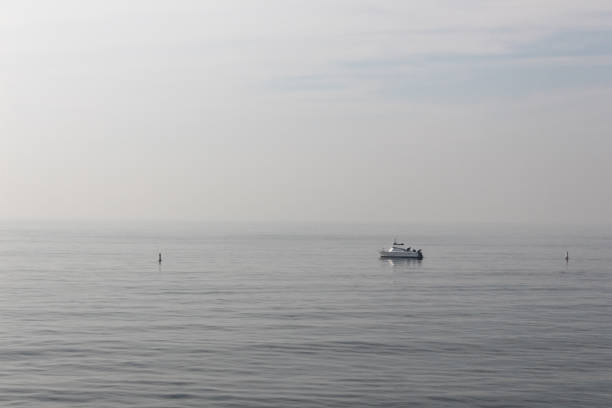 Single boat on calm ocean water on hazy morning, horizontal aspect