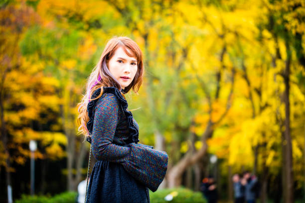An Asian female model in autumn leaves colors background, wearing black dress.