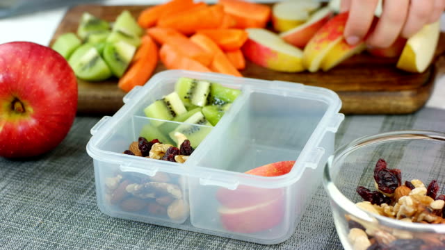 Woman hand put healthy fruit and nut snacks into the lunch box and close it