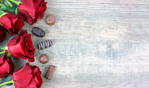 Valentine's Day Red Roses Over Wooden Background With Chocolate Candy Pieces Valentine's Day Red Roses Over Wooden Background With Chocolate Candy Pieces, Horizontal, Copy Space rose bouquet red table stock pictures, royalty-free photos & images