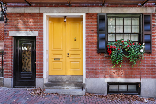 Yellow front door that is secured with potted plants in the window sill