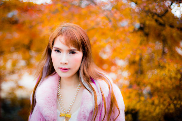 An Asian female model in autumn leaves colors background, wearing pink fur.