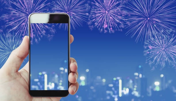 istock Hand holding mobile smart phone, blue  fireworks and Bokeh light background 902756882