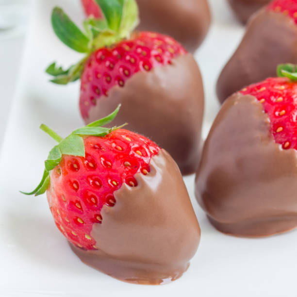 istock Strawberries covered with milk chocolate on a white plate, closeup, square format 902757278