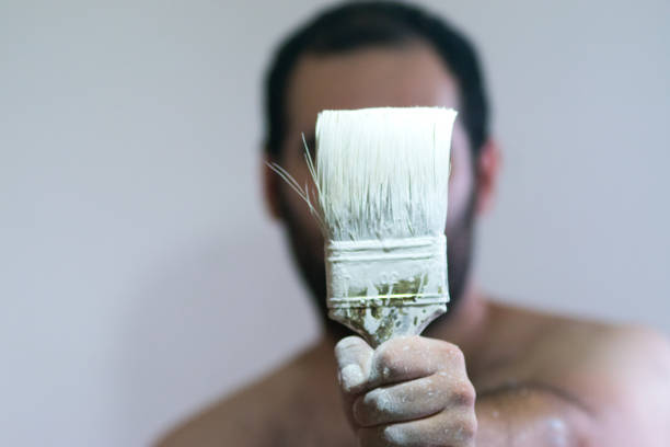 istock Man holding an old paint brush with white paint 902767672