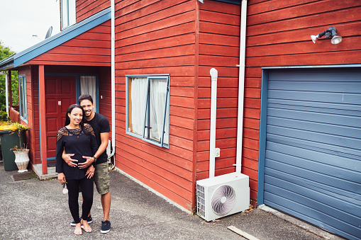 Young couple with pregnant woman in front of house they recently bought in Auckland, New Zealand.