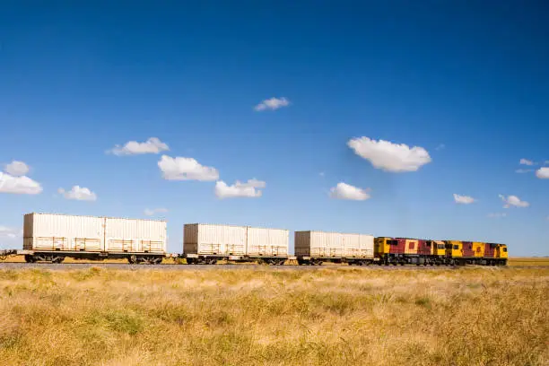 Shipping containers being hauled by a diesel engine across the dry grasslands of Queensland, Australia.