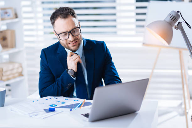 istock Tired young manager touching his tie while looking at the laptop 902793380