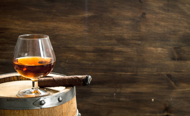 istock glass of cognac with a cigar on a barrel. 902794462