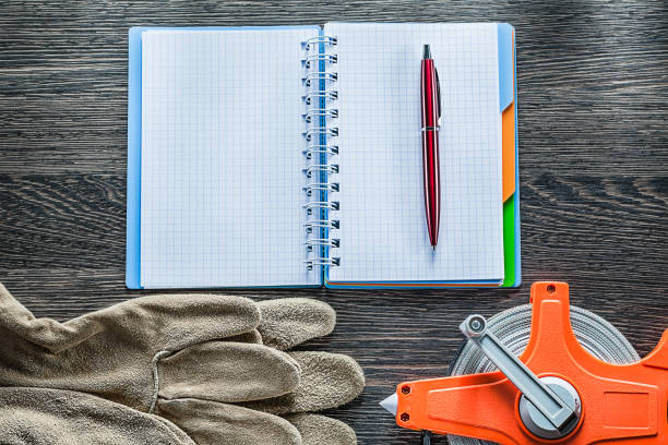 istock Construction tape measure safety gloves notebook pen on wooden b 902797218
