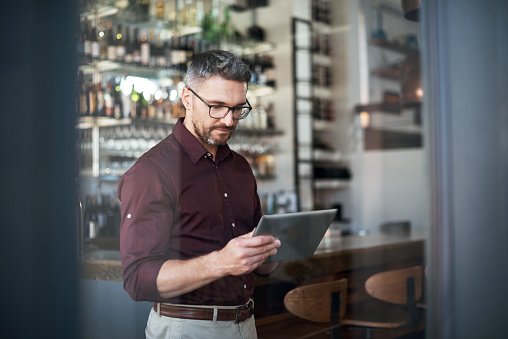 Cropped shot of a handsome businessman using a tablet while standing in his coffee shop