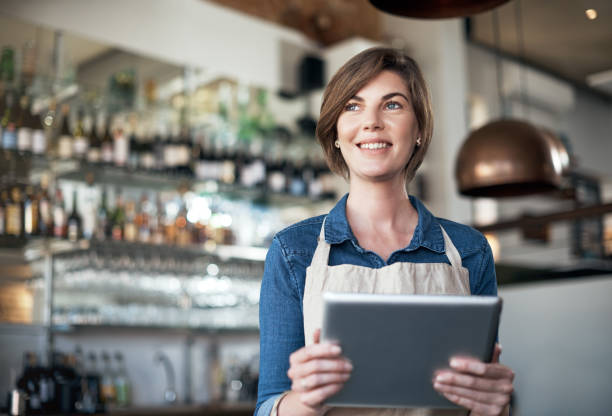 She's got some ideas for her coffee shop Cropped shot of an attractive female barista working on a tablet while standing in her coffee shop apron photos stock pictures, royalty-free photos & images