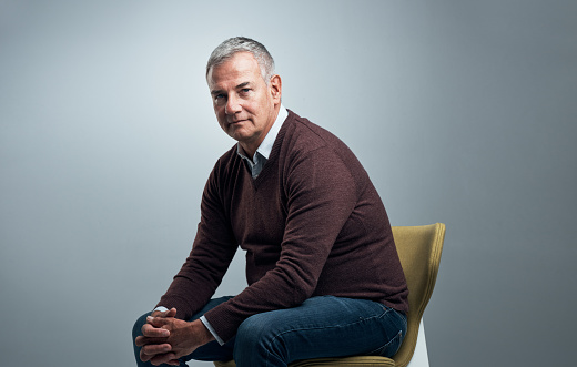 Studio shot of a handsome mature man sitting on a chair against a grey background
