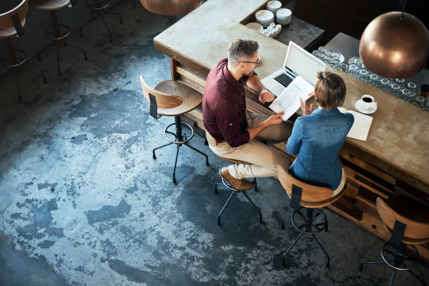 Getting work done at their local coffee shop High angle shot of two businesspeople working at the bar in a cafe business stock pictures, royalty-free photos & images