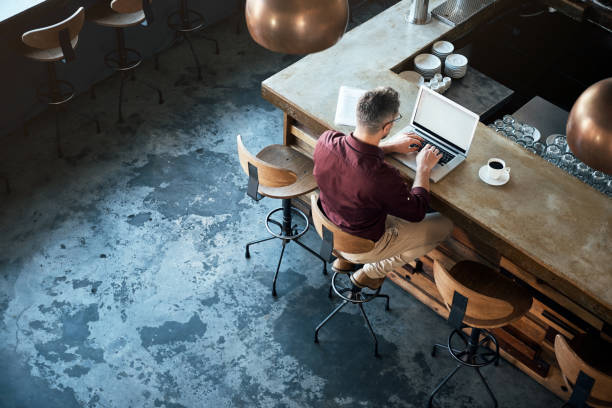 He enjoys working remotely High angle shot of a businessman working on his laptop at the bar in a cafe coffee shop stock pictures, royalty-free photos & images
