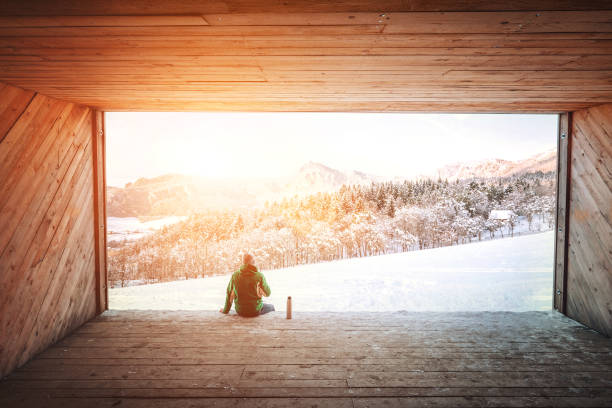 Man sits in wooden hangar wit view on snowy  mountain valley