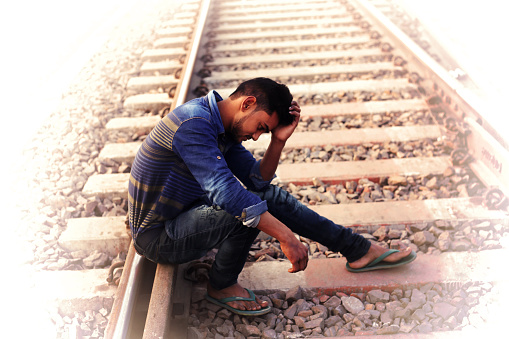Young man of Indian ethnicity in emotional stress. He is sitting on railroad track.